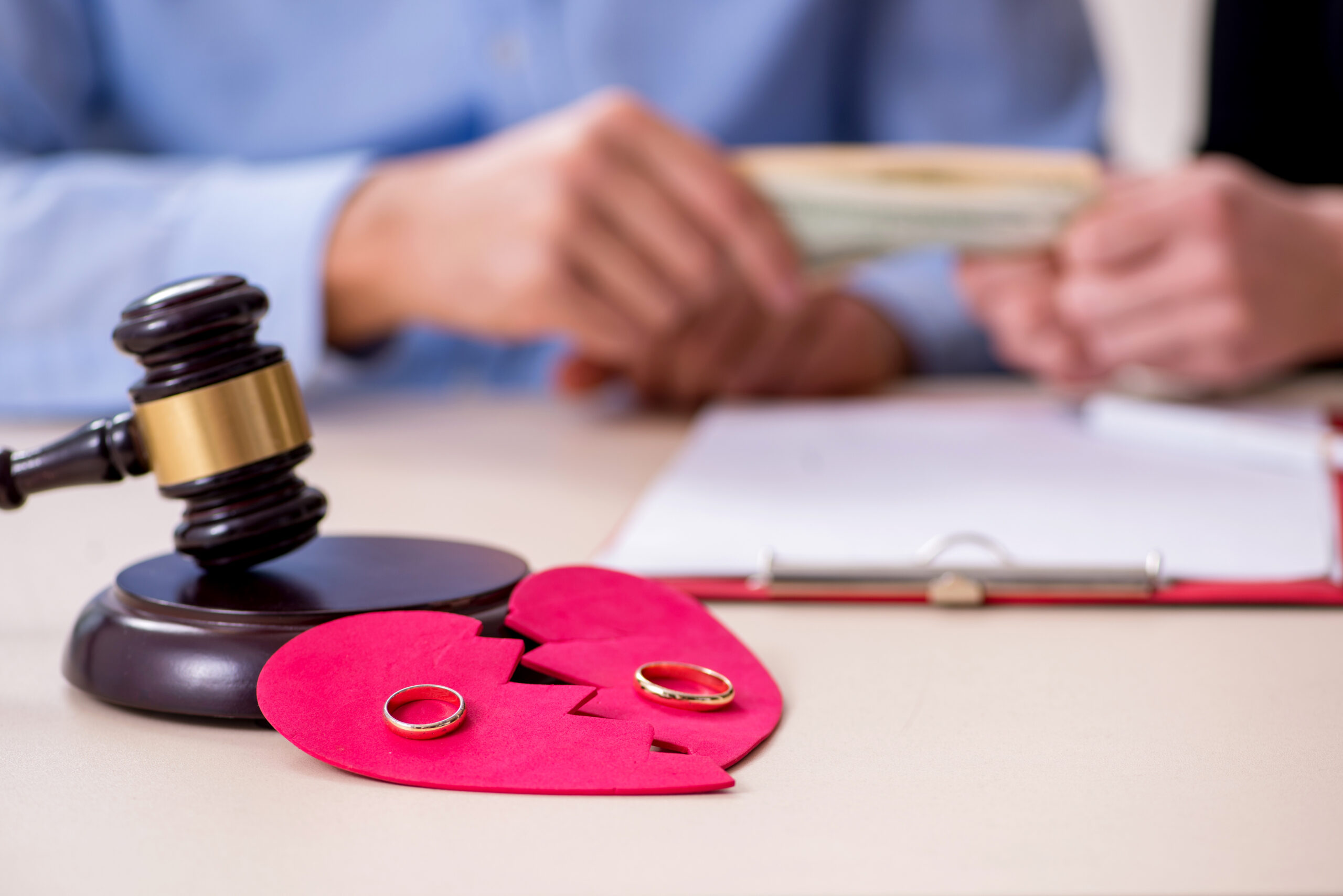 Two golden wedding rings on a broken paper heart near a judge's gavel.